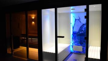 Een moderne hotelkamer met een glazen scheidingswand, een bed en een wandgemonteerde televisie die een blauwe, aquatische scène toont.
