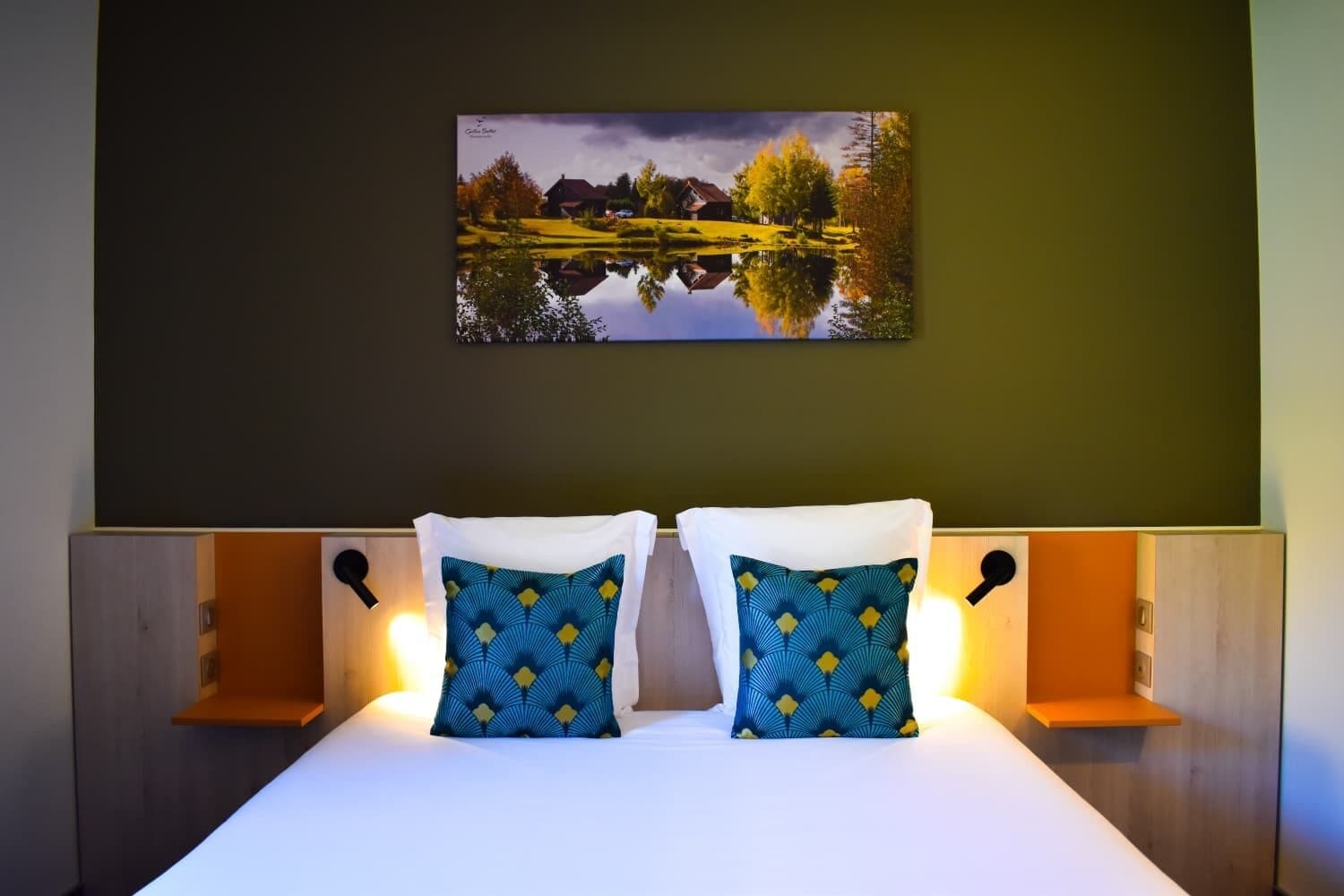 Ein Hotelzimmer mit einem Bett, zwei Zierkissen, einem Wandbild und Nachttischlampen.