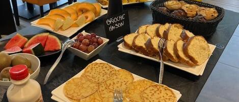 A buffet table with various breakfast items including pancakes, bread, and fruits.