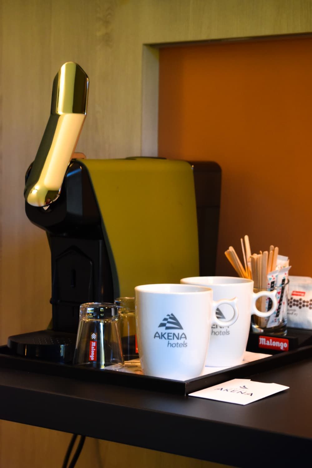 Ein Schreibtisch mit Kaffeemaschine, zwei Tassen, einem Glas und einer Ablage mit Namensschild und Stifthalter.