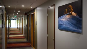 Pasillo de hotel con escaleras alfombradas, puertas y un cuadro de un paisaje nevado.