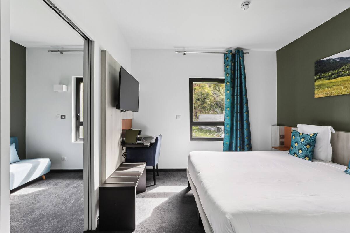 A modern hotel room with a bed, desk, and TV.