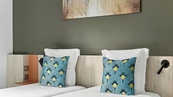Een hotelkamer met twee bedden, elk voorzien van witte lakens en gestreepte kussens.