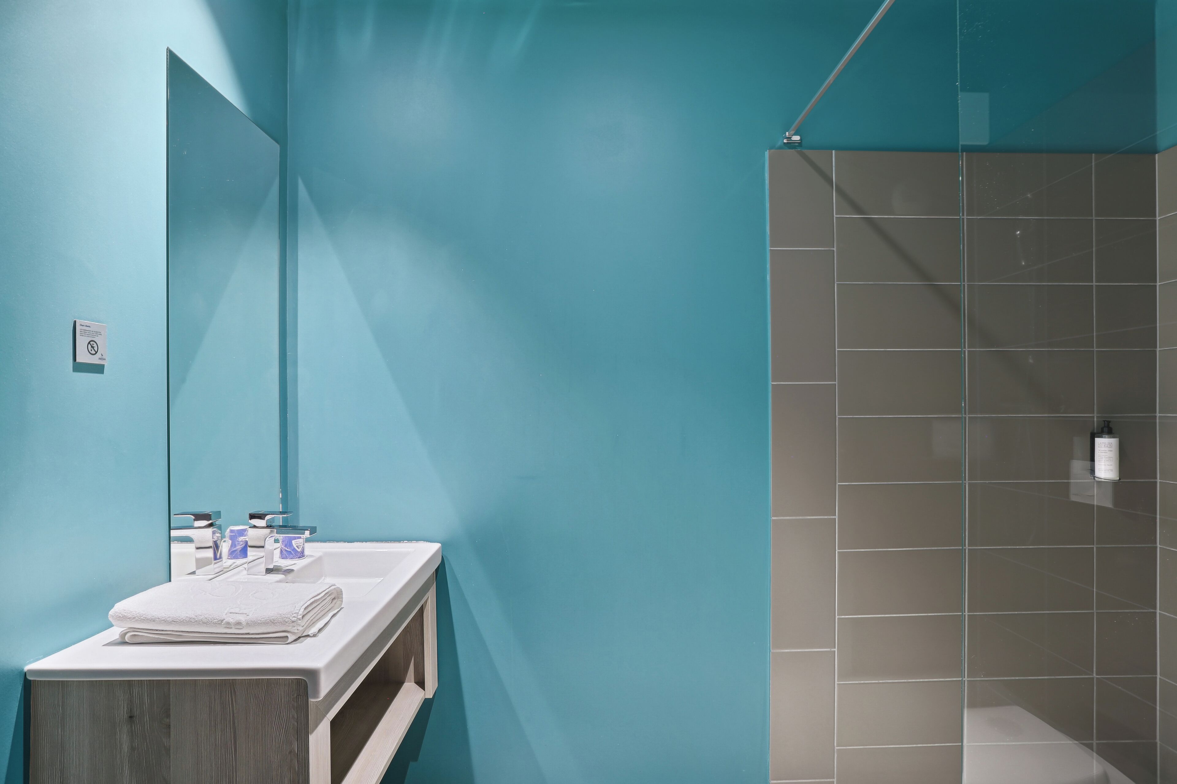 Ein Badezimmer mit einer türkisfarbenen Wand, einem weißen Waschbecken und einer Duschkabine.