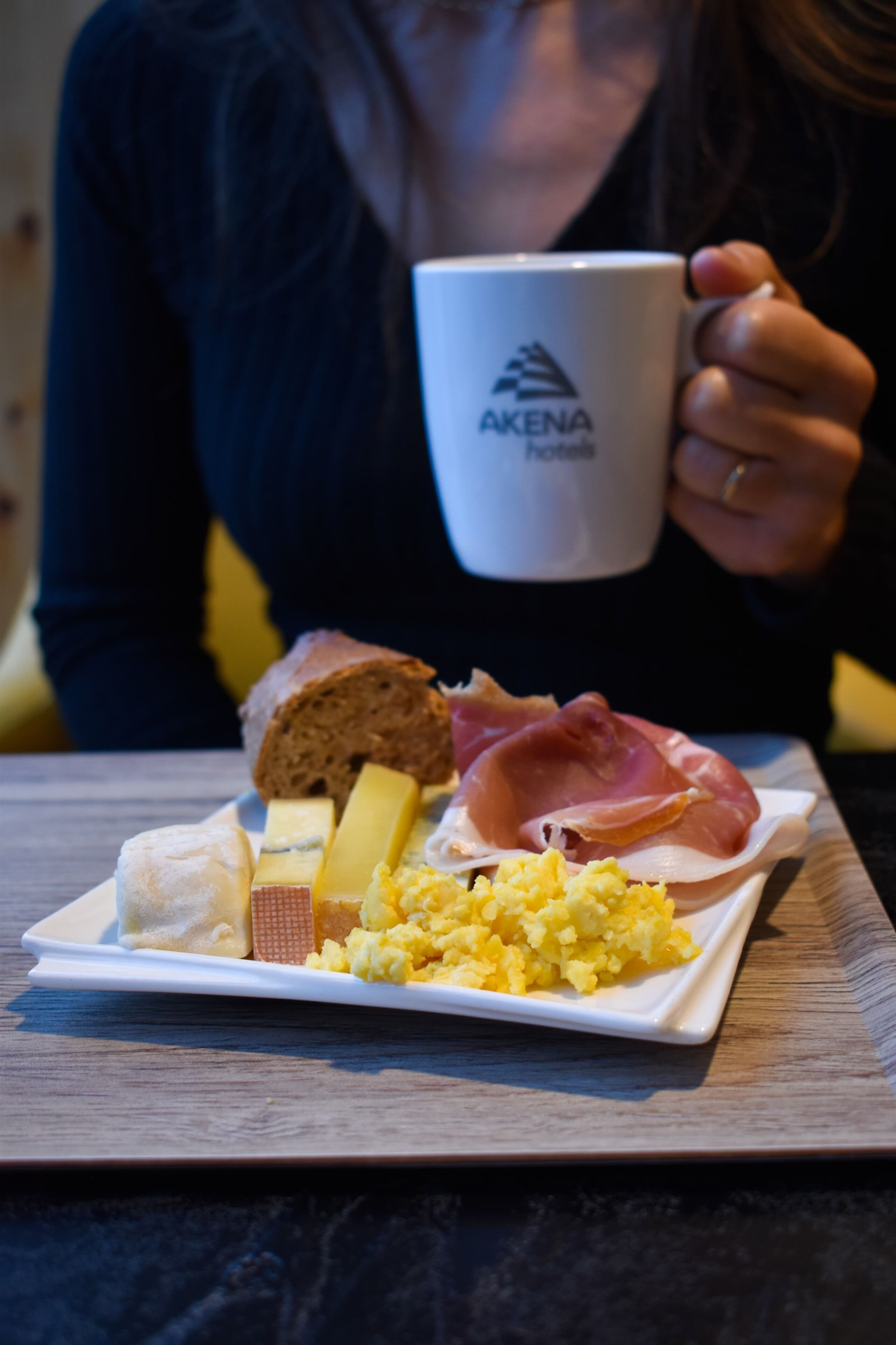 A plate with various foods including bread, cheese, ham, and scrambled eggs, held by a person.