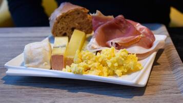 A plate with various foods including bread, cheese, ham, and scrambled eggs, held by a person.
