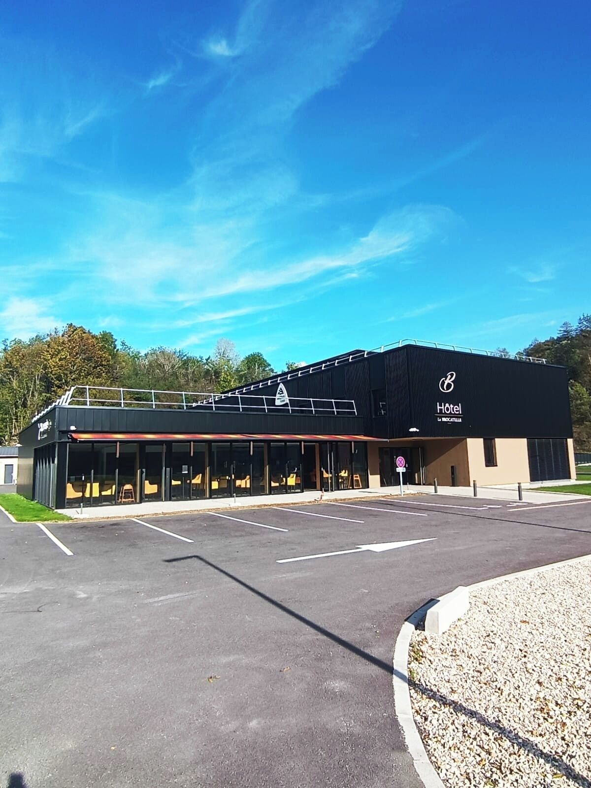 Un hôtel moderne à la façade noire, doté de grandes fenêtres et d’un parking.