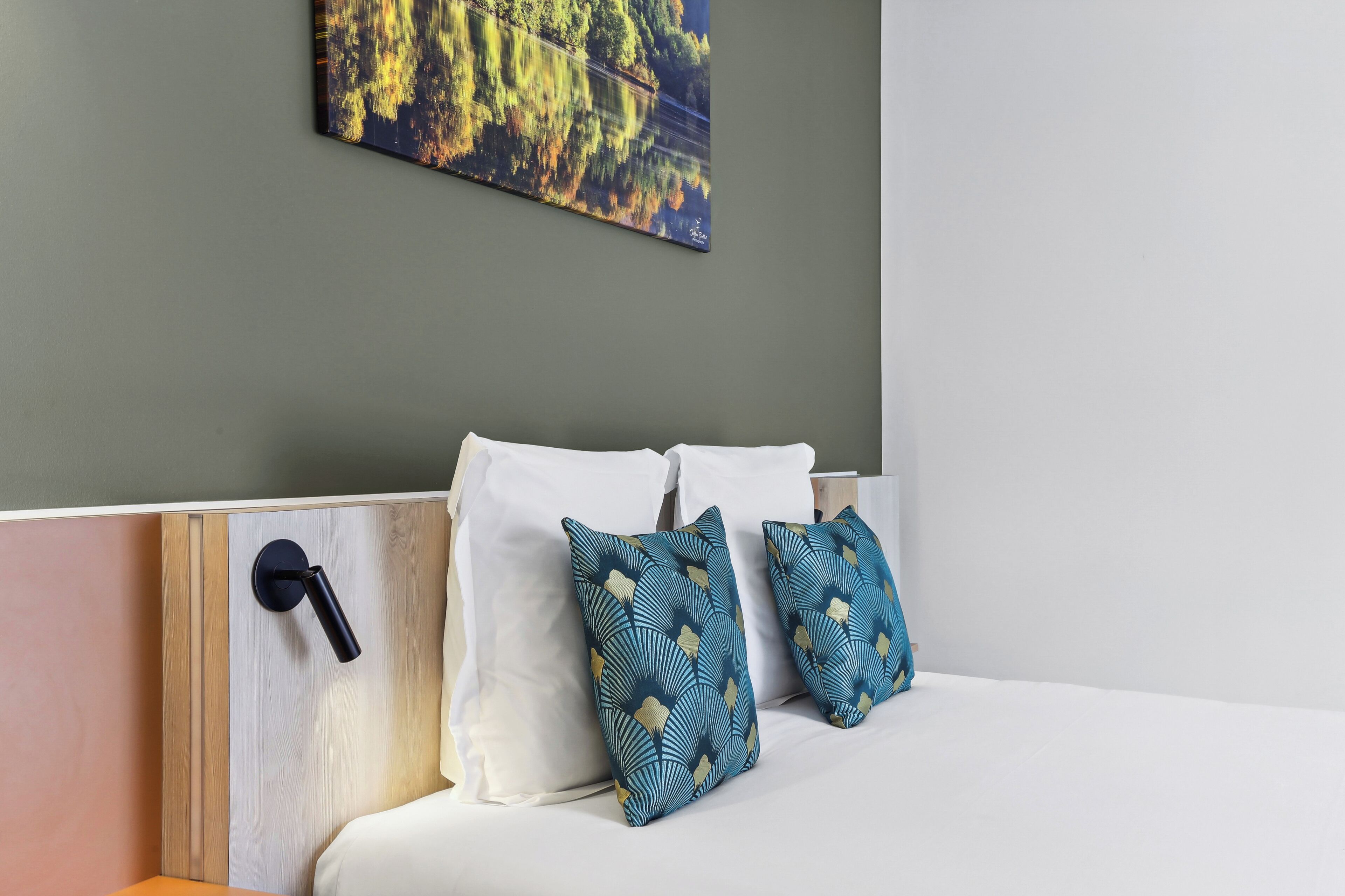 A hotel room with a bed, white pillows, and a wall-mounted artwork.
