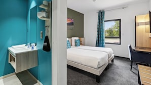 Una habitación de hotel con baño, cama, escritorio y ventana.