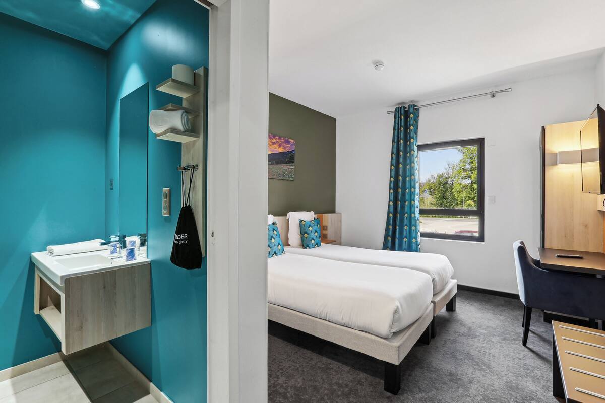 A hotel room with a bathroom, a bed, a desk, and a window.