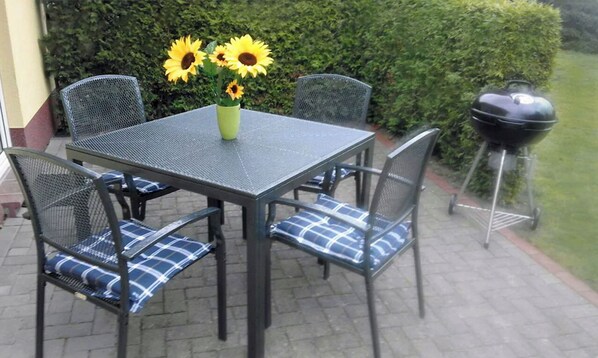 An outdoor patio with a table and chairs, a vase with sunflowers, and a barbecue grill.