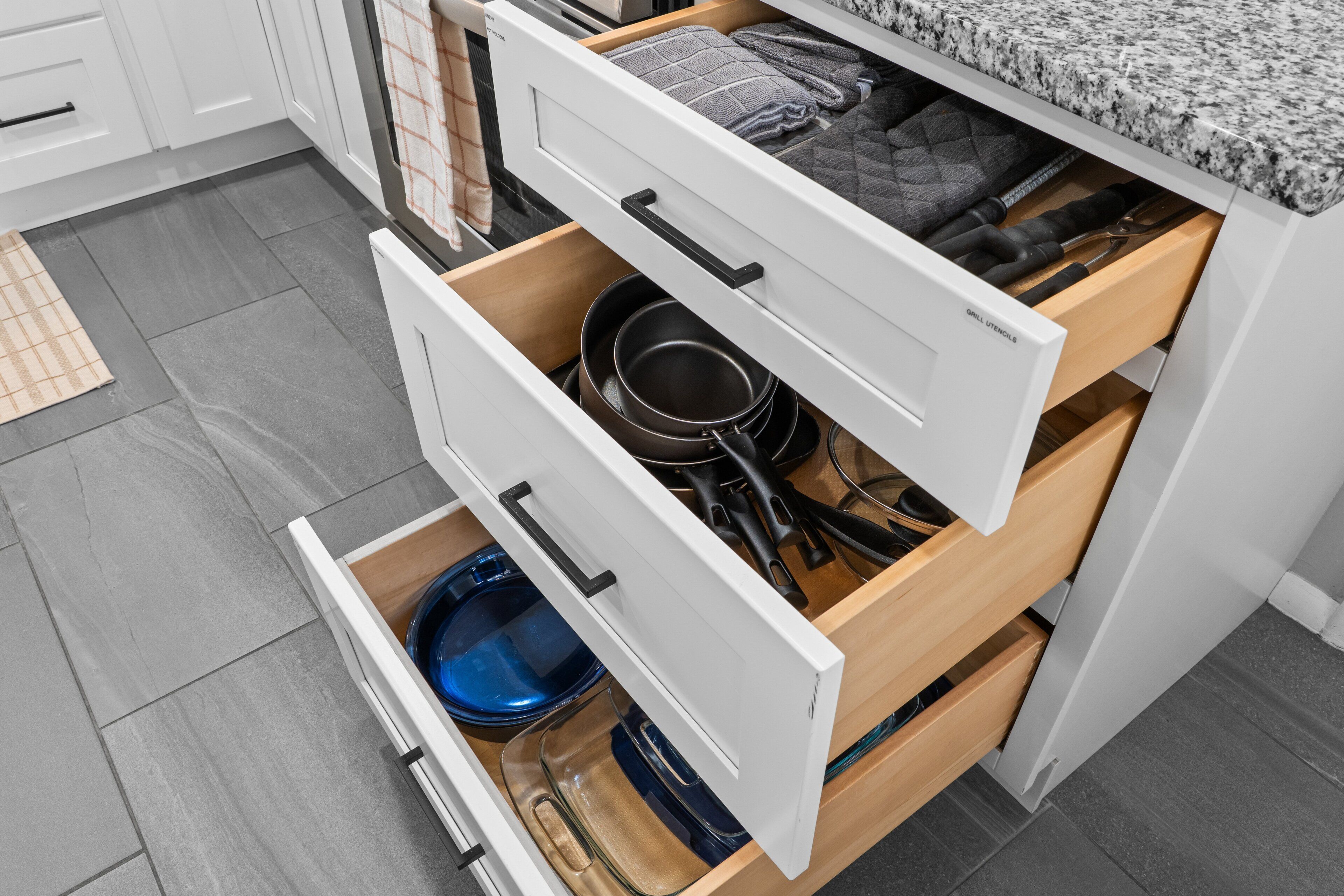 A kitchen with white cabinets, a granite countertop, and a drawer with cookware.