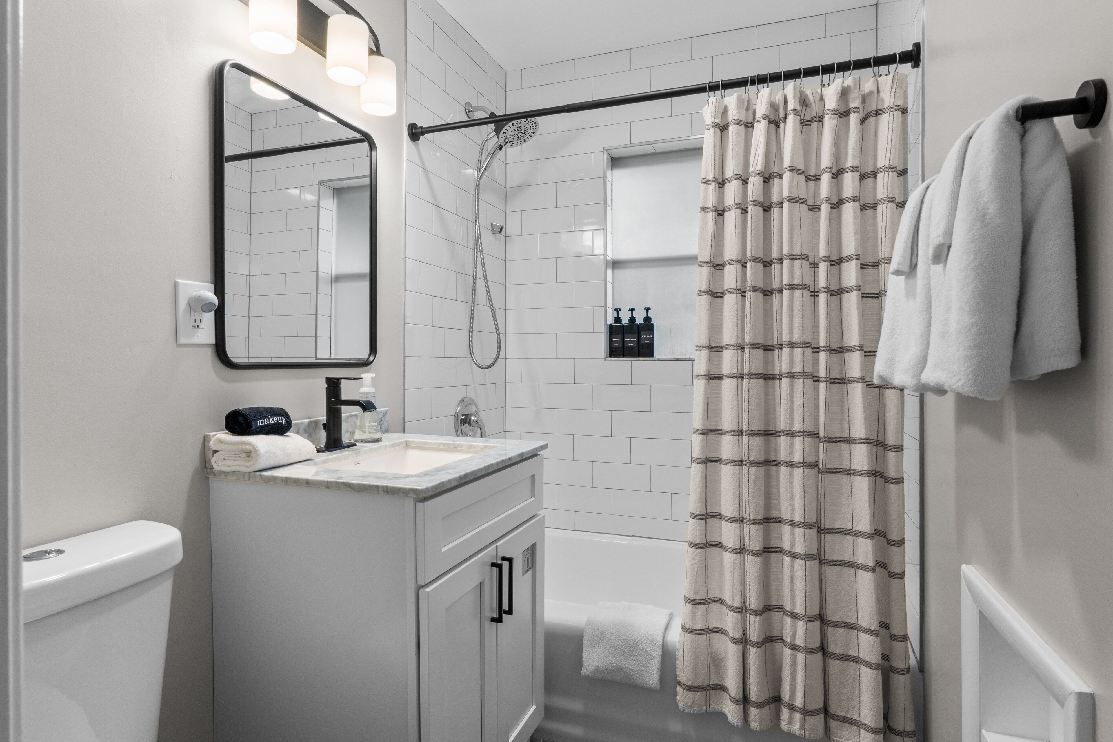 A modern bathroom with a white vanity, a mirror, a shower, and a striped shower curtain.
