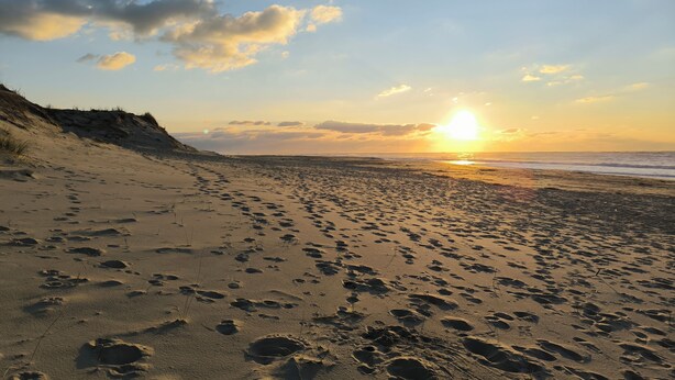 Een strand met voetafdrukken en een ondergaande zon.