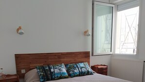 Een slaapkamer met een houten hoofdbord, een groot bed met een geweven plaid, twee nachtkastjes en een raam met uitzicht.