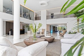 A spacious, modern lobby with a high ceiling, a central seating area with sofas and a coffee table, and a reception desk.