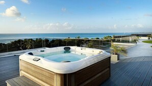 A hot tub on a wooden deck with a view of the ocean.