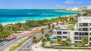 A coastal hotel with a view of the ocean, a parking lot, and a road with palm trees.