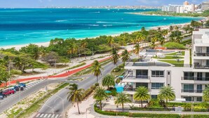 Un hotel costiero dal design moderno, con una strada che conduce alla spiaggia, palme e vista sull'oceano.