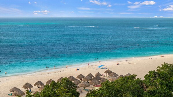 A beach with clear turquoise water, a sandy shore, and thatched umbrellas.