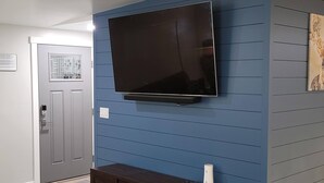 A room with a mounted flat-screen TV, a dark wooden entertainment unit, and a blue paneled wall. - Updated 2bd/2ba. Walk to Village, dog friendly, SHARC passes. (Sunriver)