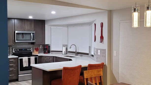 A modern kitchen with a central island, dark cabinetry, stainless steel appliances, and a dining area with wooden chairs and a table. - Updated 2bd/2ba. Walk to Village, dog friendly, SHARC passes. (Sunriver)