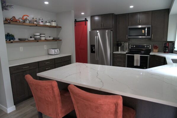 A modern kitchen with a marble countertop, stainless steel appliances, and dark wooden cabinets.