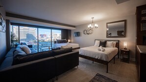 Habitació d'hotel moderna amb una finestra gran, un sofà, dos llits, una làmpada de cristall i un mirall.