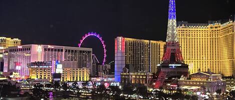 A nighttime view of a cityscape with illuminated landmarks including a tall tower and a Ferris wheel.