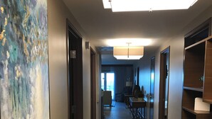 A hotel hallway with a large abstract painting on the left, a conference room in the center, and wooden shelving units on the right.