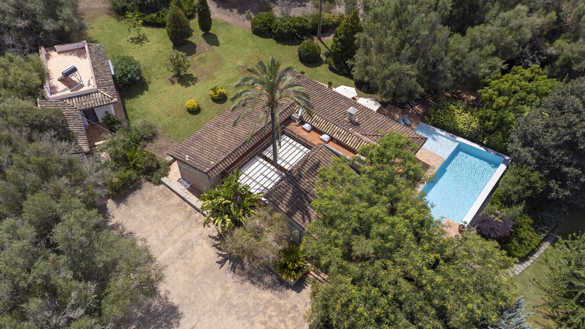 An aerial view of a property with a swimming pool, a patio area, and a small building with a tiled roof.
