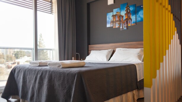 A hotel room with a large bed, a view of the city, and a painting on the wall. - DFC COLIVING (Salta)