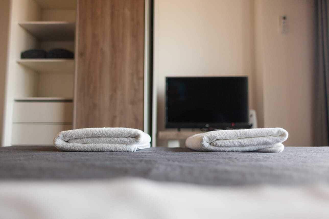 A neatly made bed with two folded towels and a television in the background.