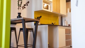 A modern kitchen with wooden cabinets, a microwave, and a small dining area with stools. - DFC COLIVING (Salta)