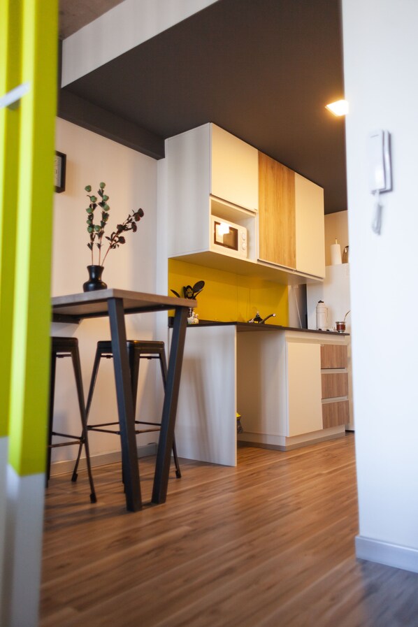 A modern kitchen with wooden cabinets, a microwave, and a small dining area with stools.