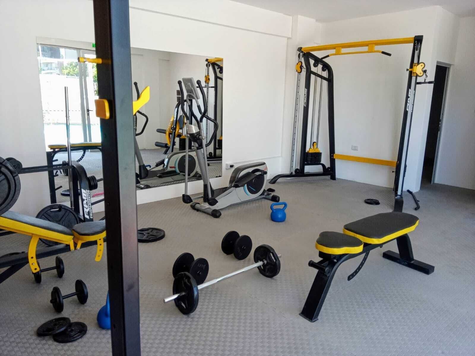 Un gimnasio con varios equipos de ejercicio, como una banca, mancuernas y máquinas de pesas.