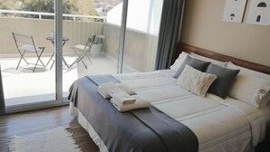 A hotel room with a large bed, a balcony with a table and chairs, and a view of the city. - DFC COLIVING (Salta)