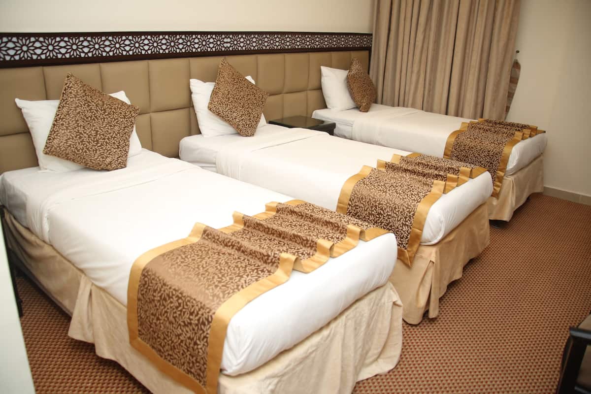 Ein Hotelzimmer mit drei Betten, jedes mit einer gemusterten Tagesdecke und passenden Kissen.