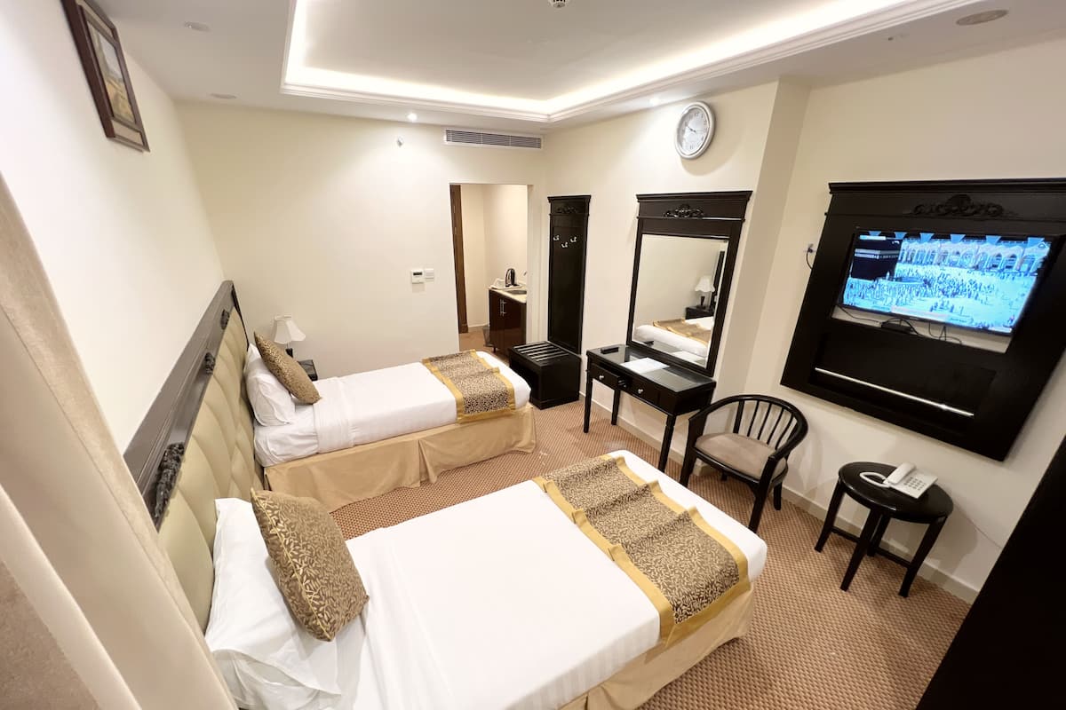 Ein Hotelzimmer mit zwei Betten, einem Schreibtisch, einem Stuhl, einem Fernseher und einem Spiegel.