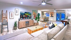 A modern living room with a large flat-screen TV, a wooden coffee table, a beige sofa, and a dining area with a table and chairs. - WOW! Luxury Desert Oasis! (Mesa)