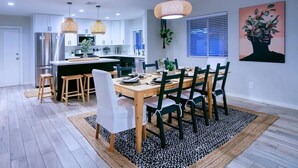 A modern kitchen with white cabinets, a stainless steel refrigerator, and a dining area with a wooden table and chairs. - WOW! Luxury Desert Oasis! (Mesa)
