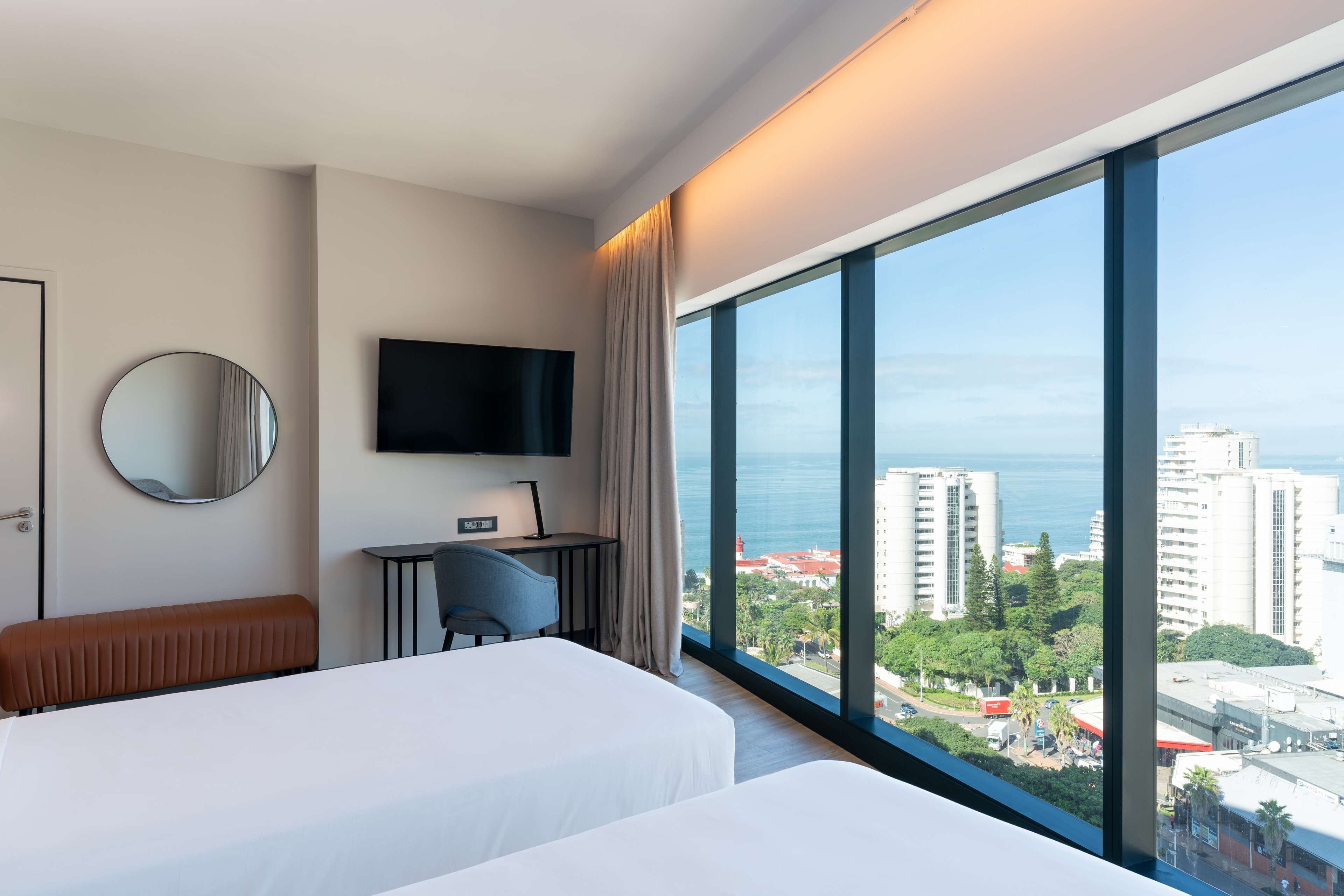 Une chambre d’hôtel avec deux lits, un bureau, une télévision et une grande fenêtre donnant sur la ville.