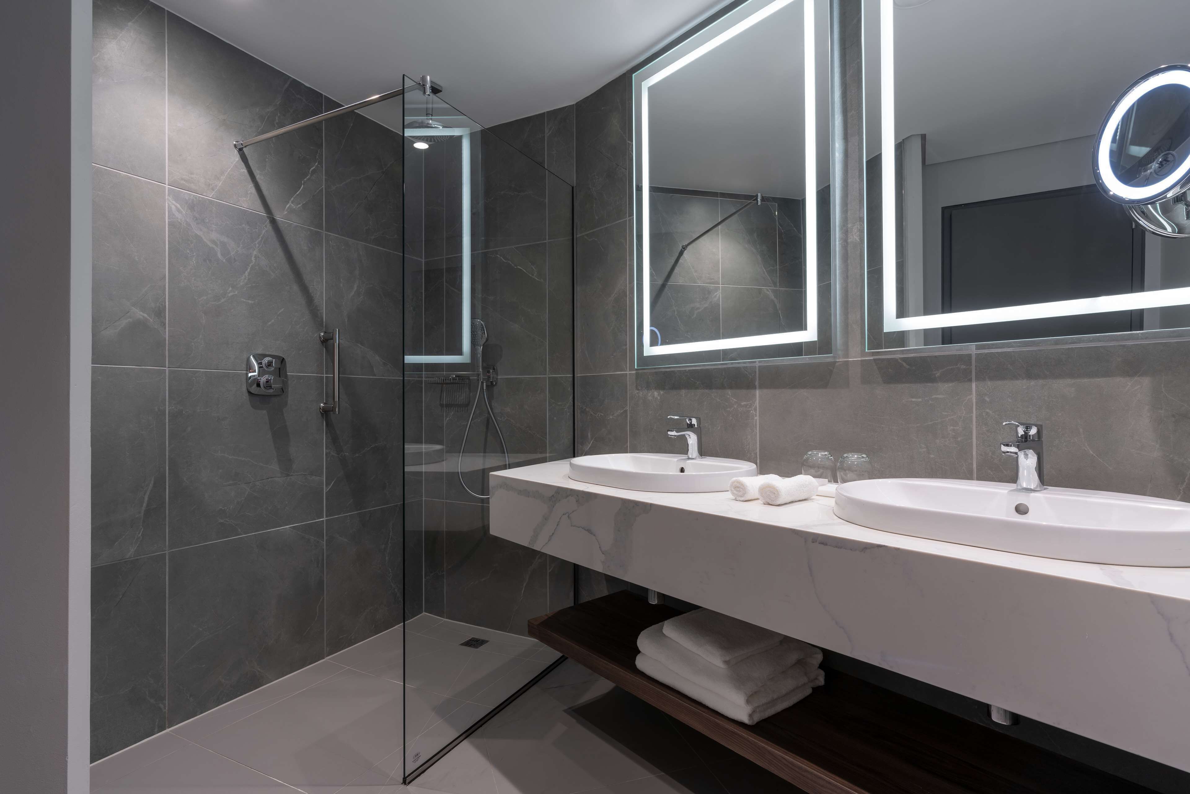Un baño moderno con dos lavamanos, cabina de ducha de vidrio y un espejo grande con luz.