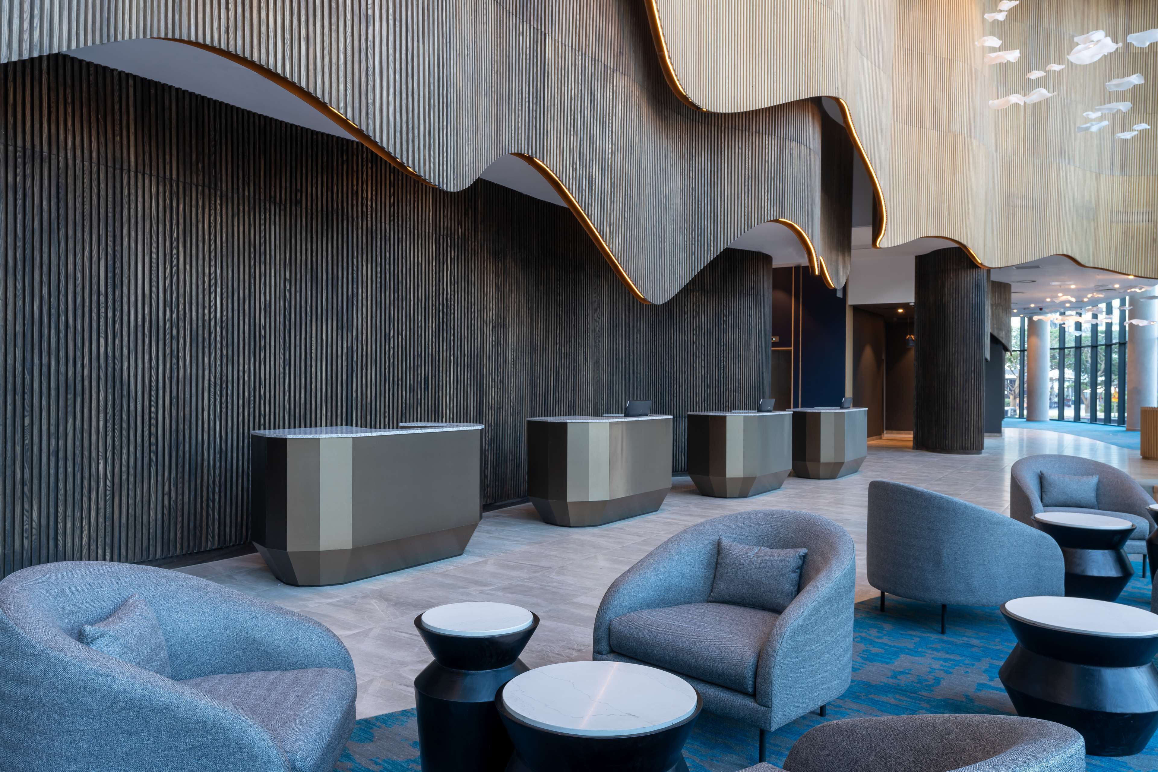 A modern lobby with seating areas, reception desks, and a patterned wall.