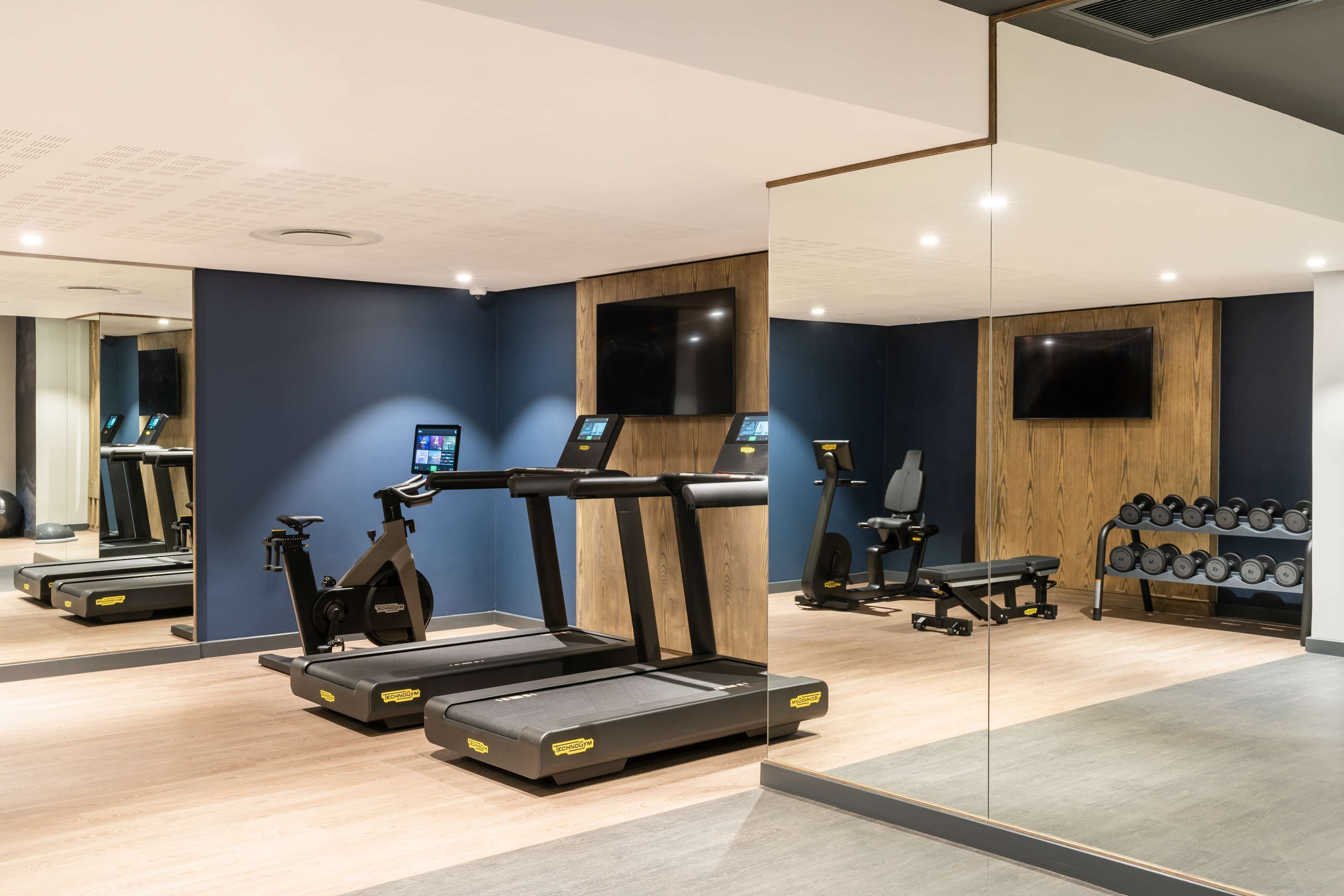 Une salle de sport moderne équipée de tapis de course, de vélos d’appartement et d’un banc de musculation.