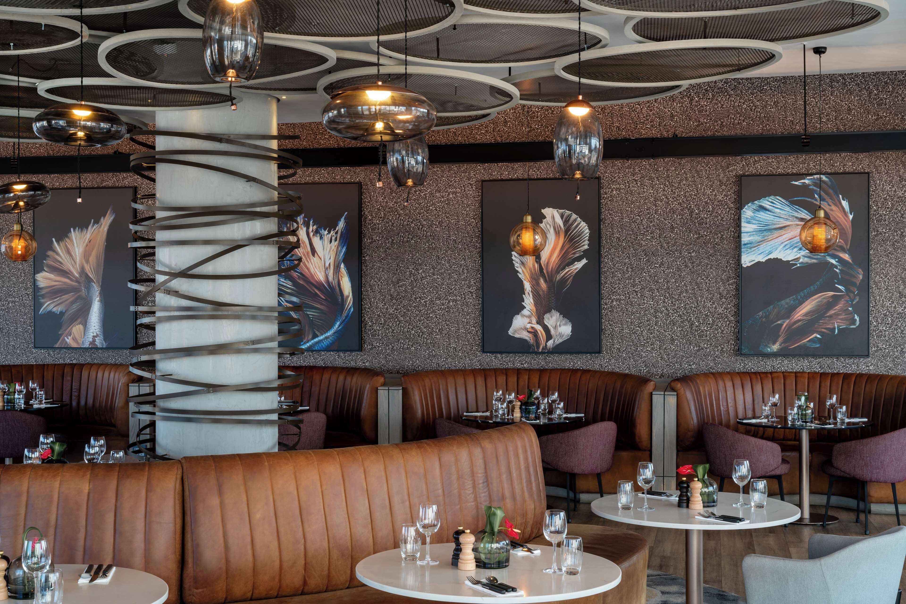 A modern restaurant interior with leather booths, round tables, and abstract wall art.