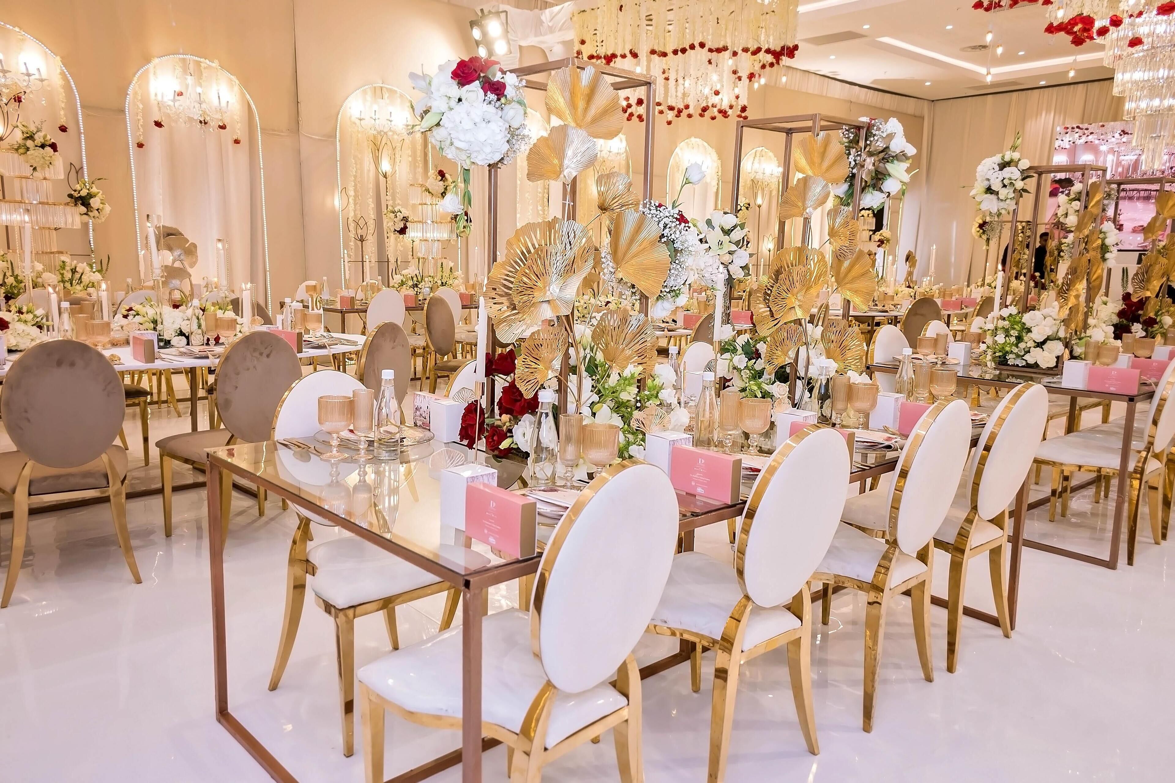 A luxurious banquet hall with mirrored walls, elegant gold and white chairs, and ornate floral arrangements.