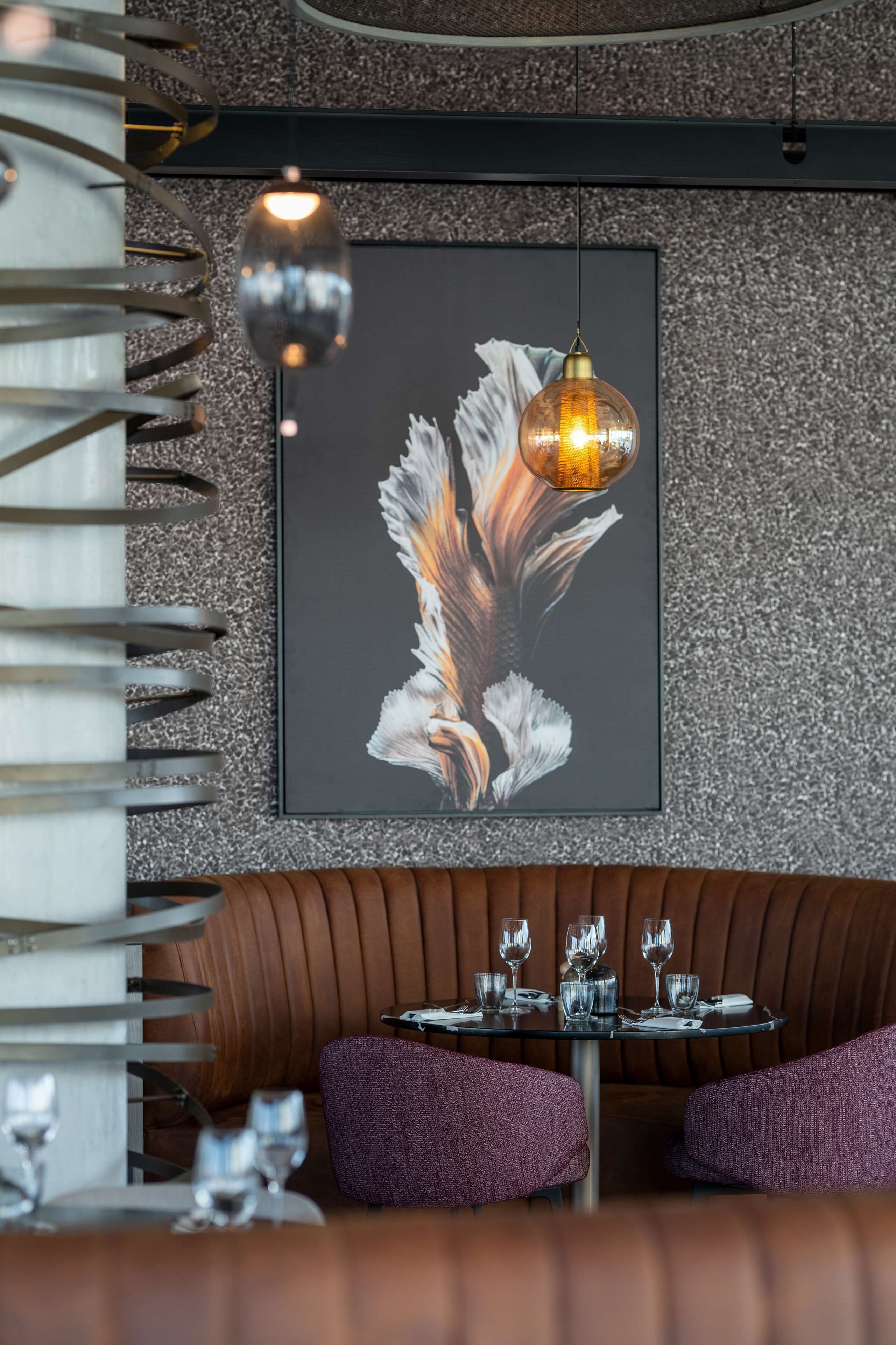 A restaurant interior with a dining table set for two, a framed artwork on the wall, and a spiral staircase.