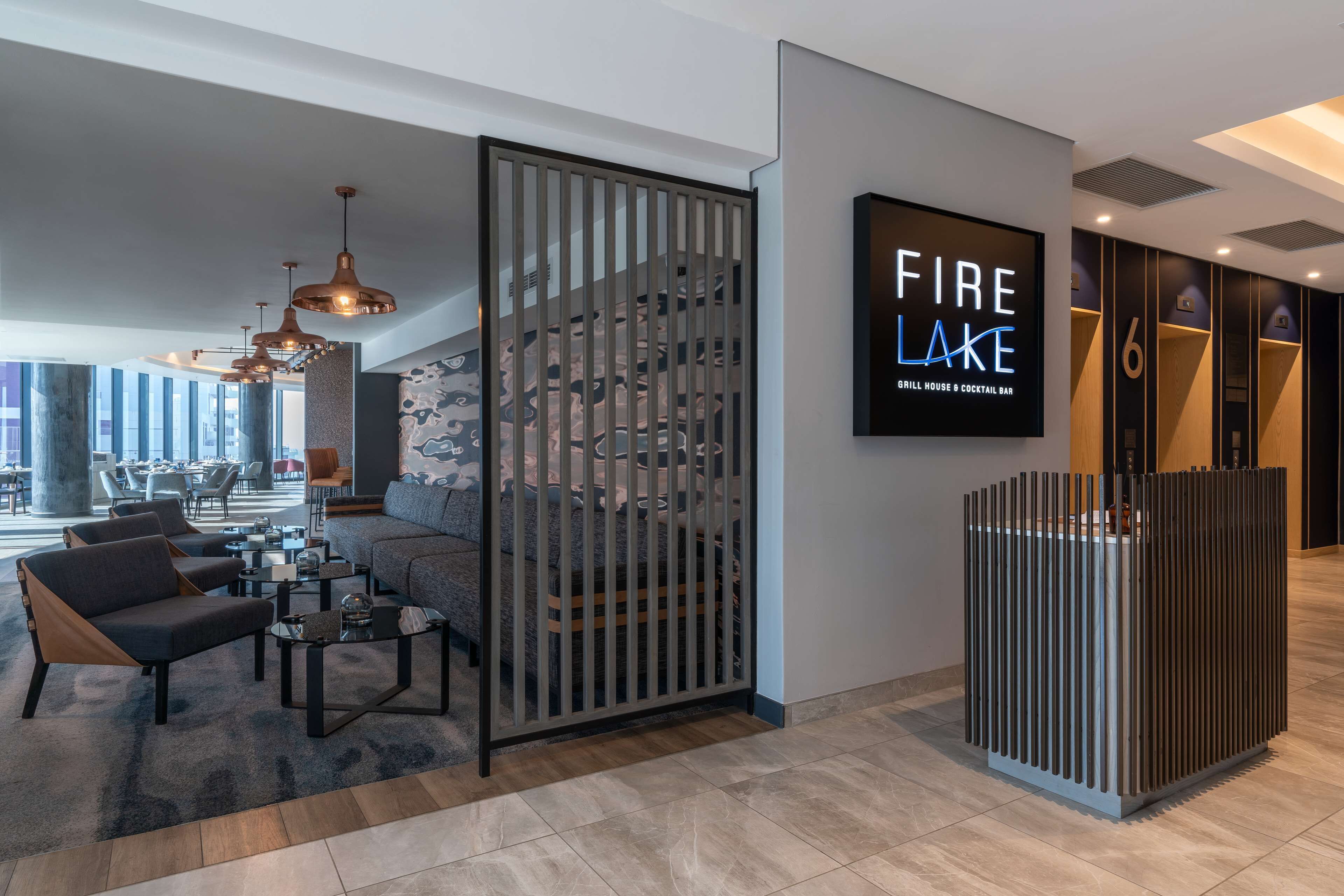 Una hall moderna di un hotel con un'area salotto, una scala e un bar chiamato "Fire Lake".