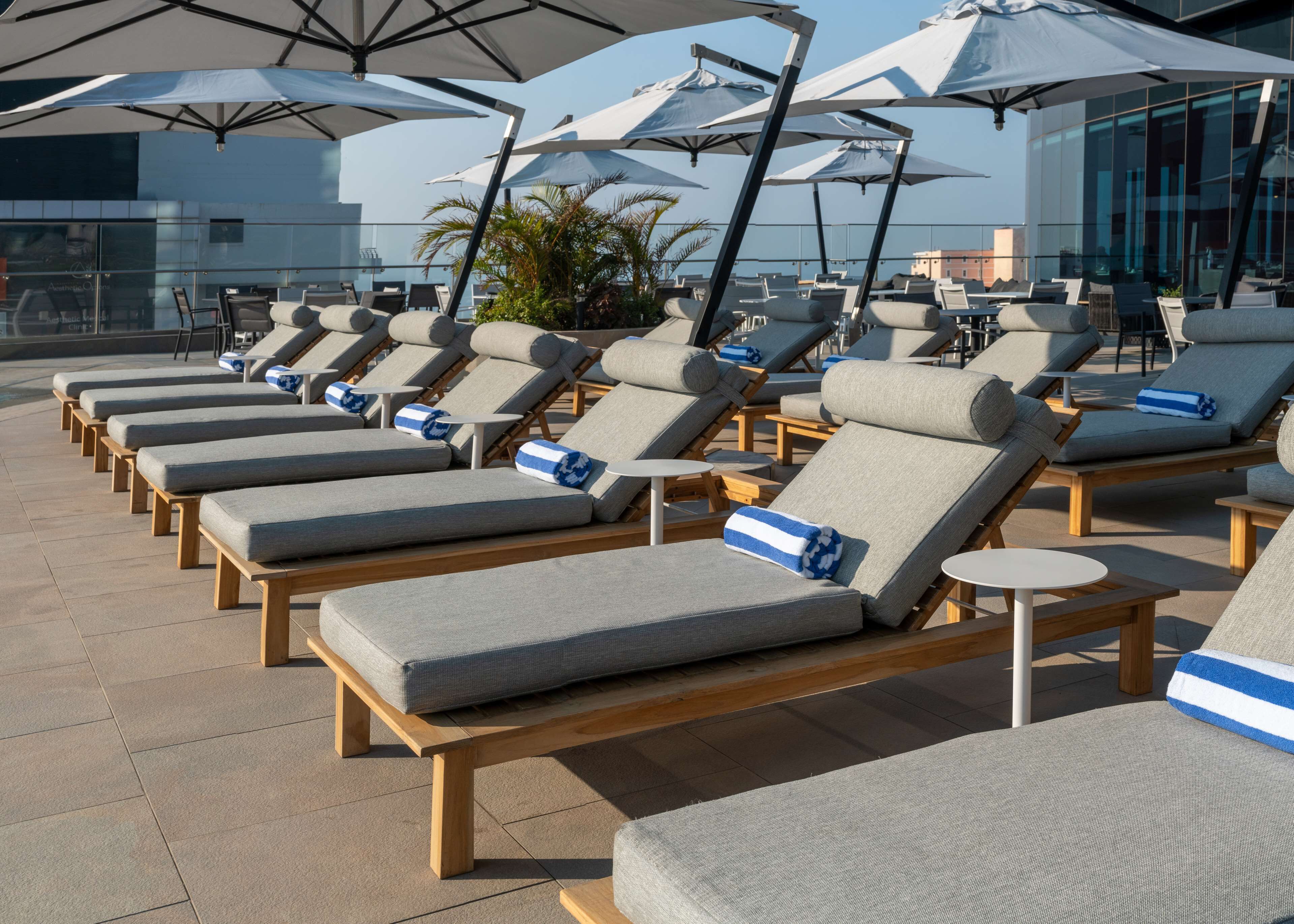 Une rangée de chaises longues avec coussins, disposées dans un espace extérieur moderne agrémenté de parasols et avec un bâtiment en arrière-plan.